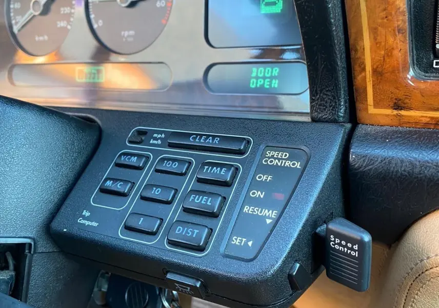 Gros plan sur le tableau de bord en bois et les commandes du cruise control d'une Jaguar XJ6 3.6 Sovereign bleu de 1987