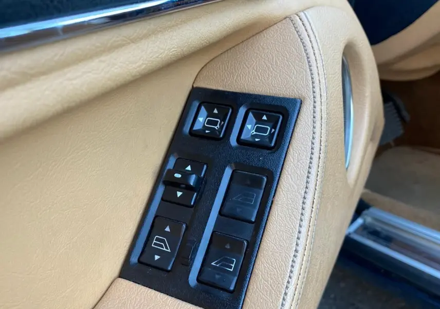Gros plan sur les commandes électriques beige de la portière côté gauche d'une Jaguar XJ6 3.6 Sovereign bleue de 1987.