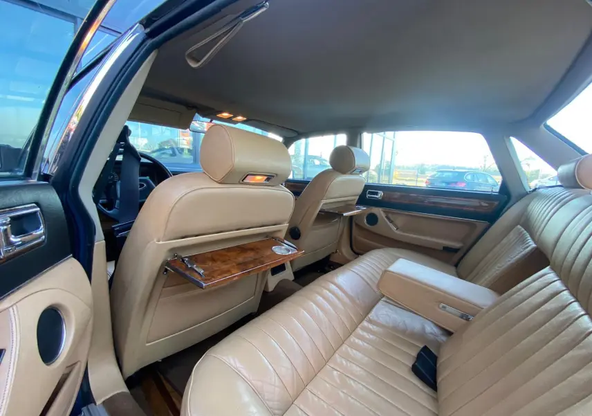 Intérieur beige cuir de la Jaguar XJ6 3.6 Sovereign 1987, vue arrière côté gauche avec tablettes en bois sur les sièges avant.