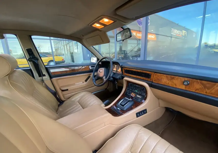 Intérieur beige clair de la Jaguar XJ6 3.6 Sovereign 1987, vue côté conducteur avec tableau de bord en bois et boîte auto.