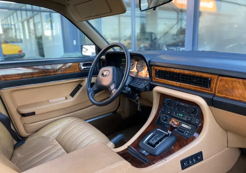 Intérieur beige et bois d'une Jaguar XJ6 3.6 Sovereign 1987, vue côté conducteur sur tableau de bord et console centrale.