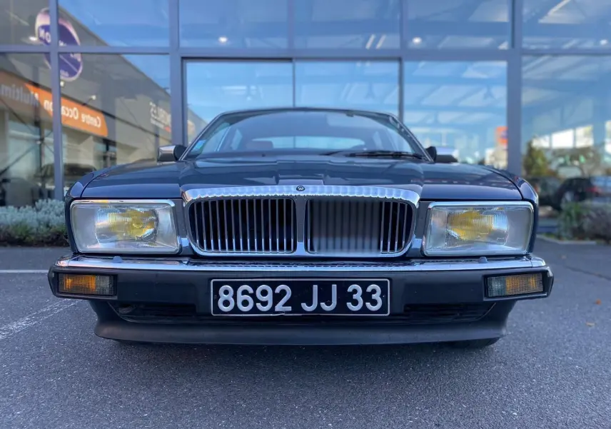 Vue frontale d'une Jaguar XJ6 3.6 Sovereign bleu de 1987 avec calandre chromée et phares jaunes.