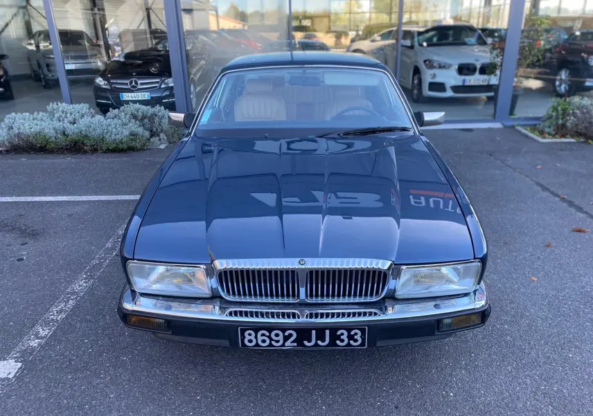 Jaguar XJ6 3.6 Sovereign bleu 1987 vue de face, avec calandre chromée et phares rectangulaires allumés.