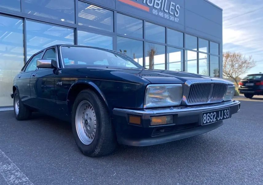 Jaguar XJ6 3.6 Sovereign bleu vue 3/4 avant avec calandre chromée et phares rectangulaires, stationnée devant un showroom.