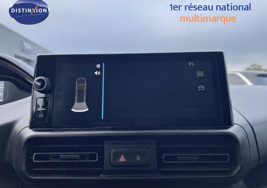 Écran tactile central du Peugeot Partner 2025 affichant l’aide au stationnement, avec les aérateurs et boutons de sécurité en dessous.