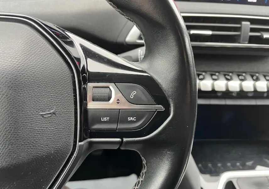 Gros plan sur le volant multifonctions en cuir du Peugeot 3008 gris Amazonite, avec commandes audio et téléphone visibles.