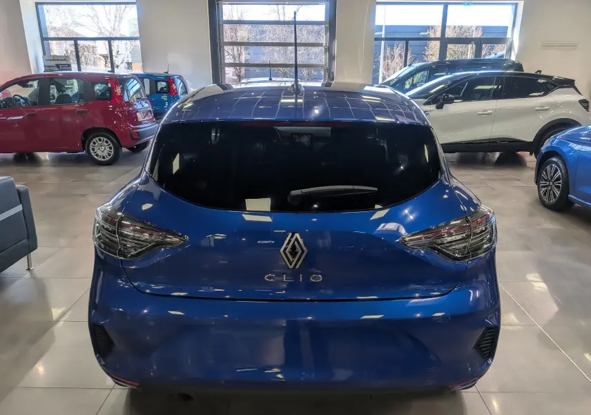 Vue arrière d'une Renault Clio V Bleu Iron 2025 avec vitres teintées et feux arrière LED en intérieur showroom.