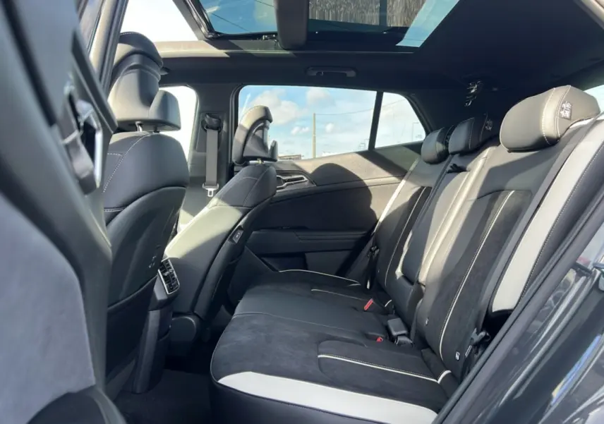 Vue intérieure arrière droite du Kia Sportage 2026 gris eclipse avec toit panoramique et sièges en cuir noir et alcantara.