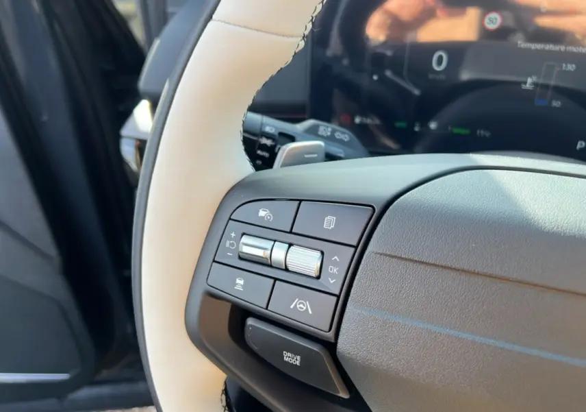 Gros plan sur le volant cuir beige du Kia Sportage 2026 avec commandes multifonctions côté gauche et tableau de bord numérique flou.