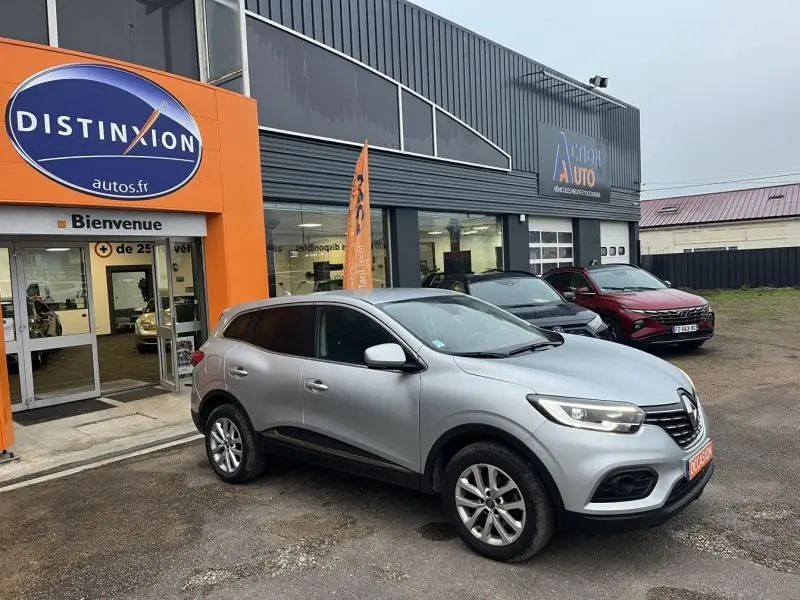 Renault Kadjar blanc en 3/4 avant droit, stationné devant un garage avec enseigne orange Distinxion.