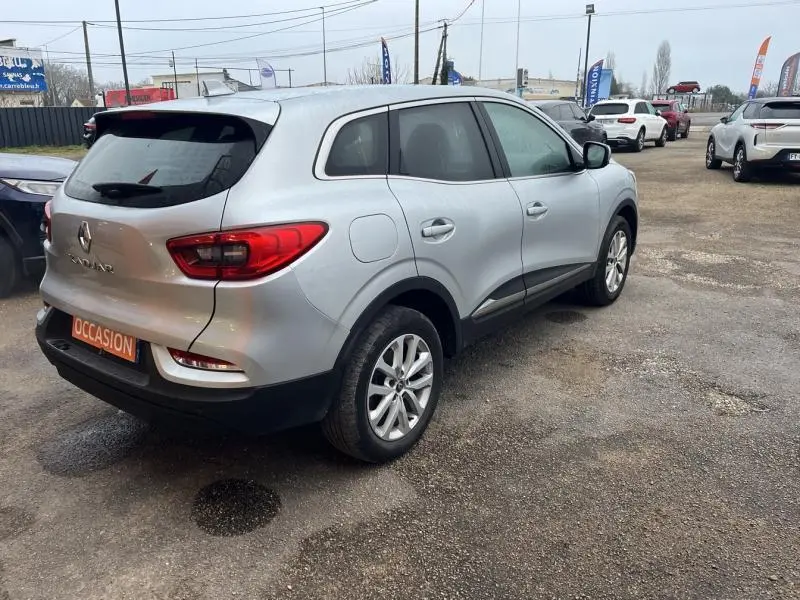 Vue 3/4 arrière droite d'un Renault Kadjar blanc glacier garé sur un parking extérieur avec plusieurs autres véhicules.