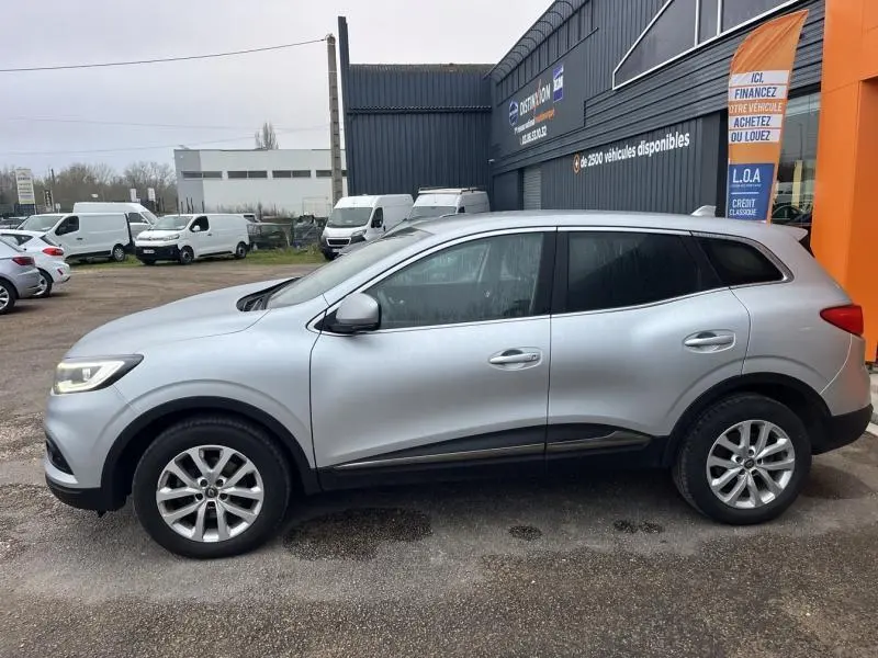 Profil côté gauche d'un Renault Kadjar blanc 2022 garé devant un bâtiment commercial avec jantes alliage.