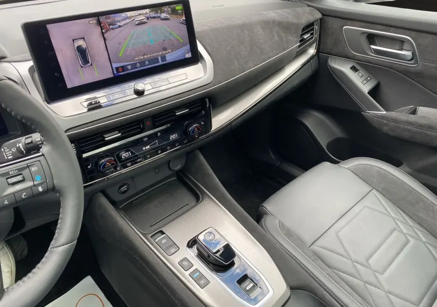 Vue intérieure côté passager du tableau de bord et console centrale du Nissan Qashqai 1.5 e-POWER 2025 en gris et noir avec écran tactile.