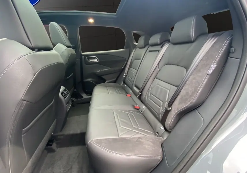 Vue intérieure arrière du Nissan Qashqai 2025, sièges en cuir noir avec surpiqûres blanches et ceintures de sécurité visibles.