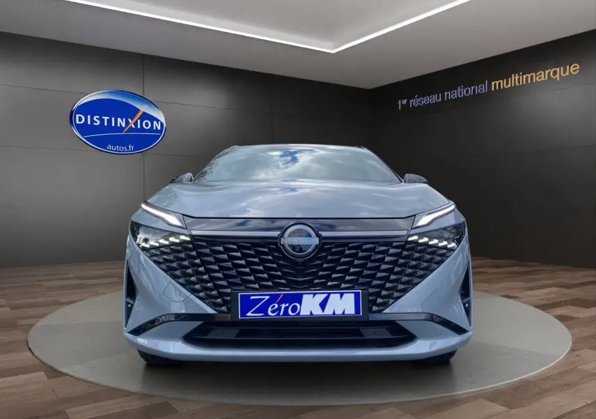 Vue frontale du Nissan Qashqai 2025 gris céramic avec calandre noire texturée et phares LED fins allumés.