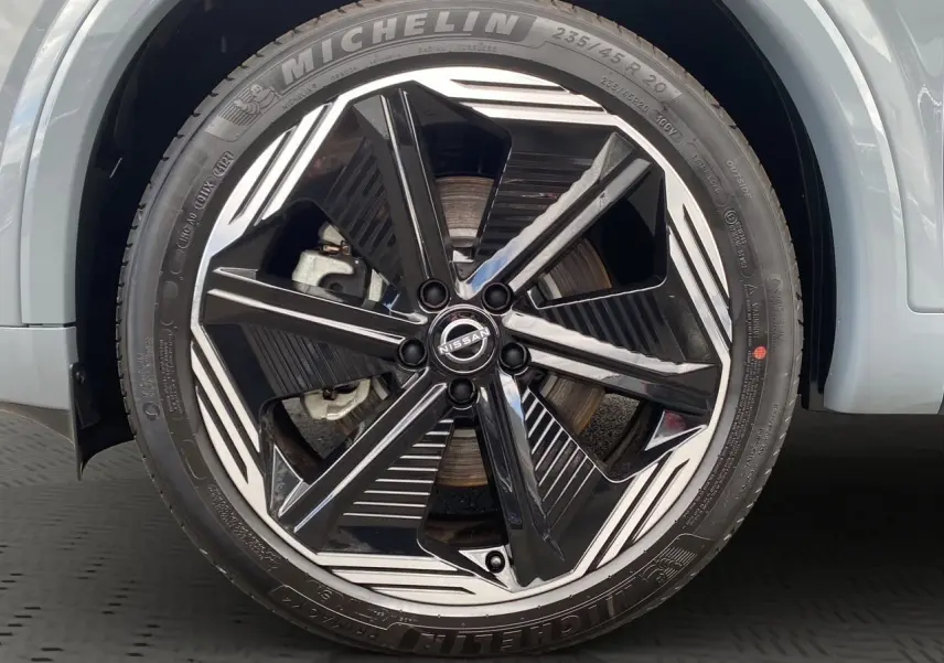 Gros plan sur la roue avant droite du Nissan Qashqai 2025 gris ceramic avec jante alliage noir et argentée au design moderne.