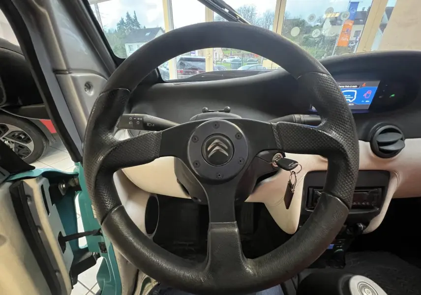 Vue intérieure centrée sur le volant noir du Citroën E-MEHARI cabriolet bleu clair avec tableau de bord et clé sur contact.