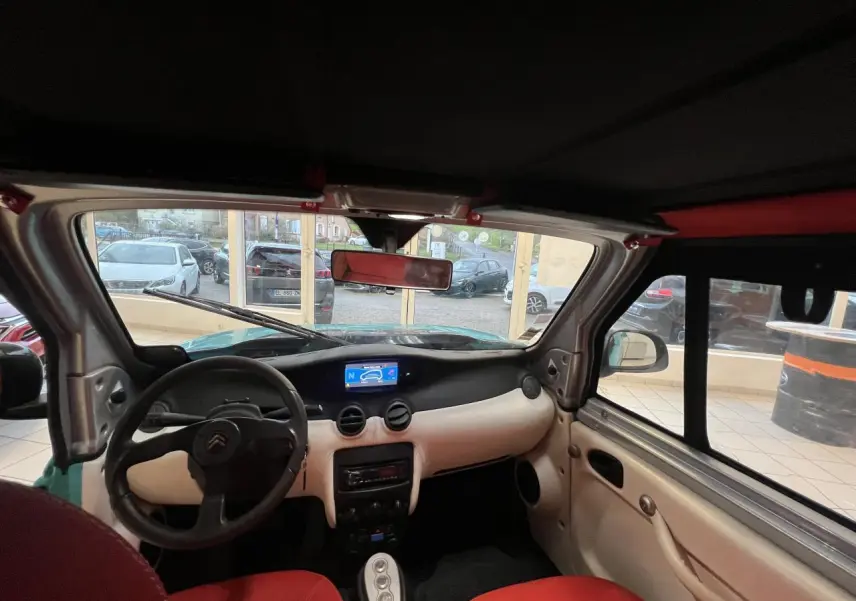 Vue intérieure avant de la Citroën E-MEHARI cabriolet bleu clair, avec tableau de bord clair et sièges rouges.