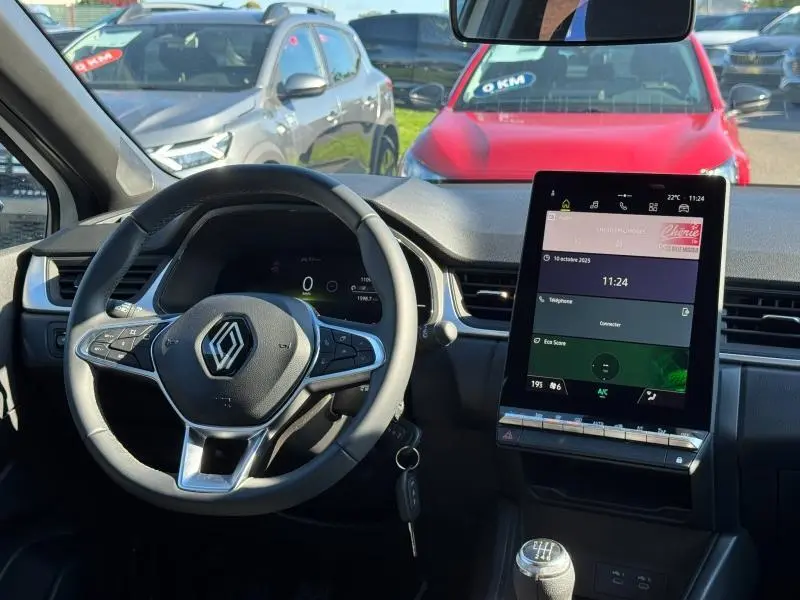 Intérieur du Renault Captur 2025 noir, vue centrée sur le volant et l'écran tactile vertical avec boîte manuelle visible.