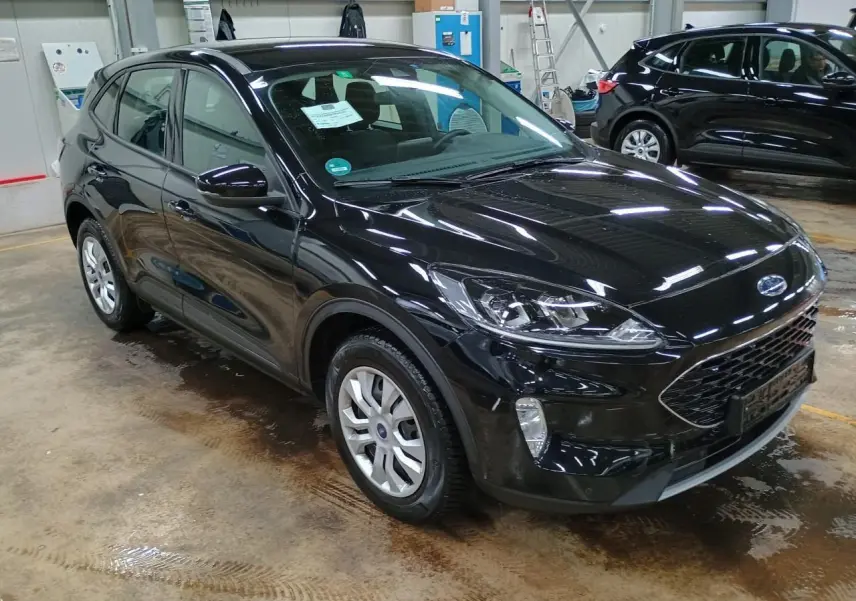 Ford Kuga noir Obsidien vu en 3/4 avant droit dans un garage, avec calandre et phares distinctifs visibles.