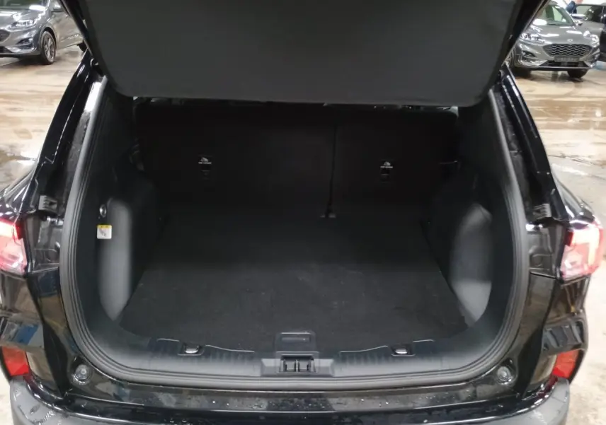 Vue arrière du coffre ouvert du Ford Kuga noir Obsidien 2024, montrant l'espace de chargement vide et les feux arrière allumés.