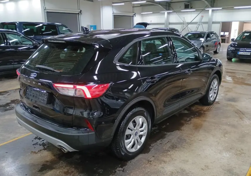 Vue 3/4 arrière droite d'un Ford Kuga 2024 noir Obsidien dans un garage, avec feux arrière allumés.