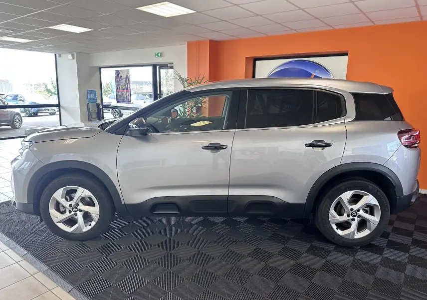 Profil côté gauche d'un Citroën C5 Aircross 2024 gris Artense avec jantes alliage et vitres arrière surteintées en showroom.