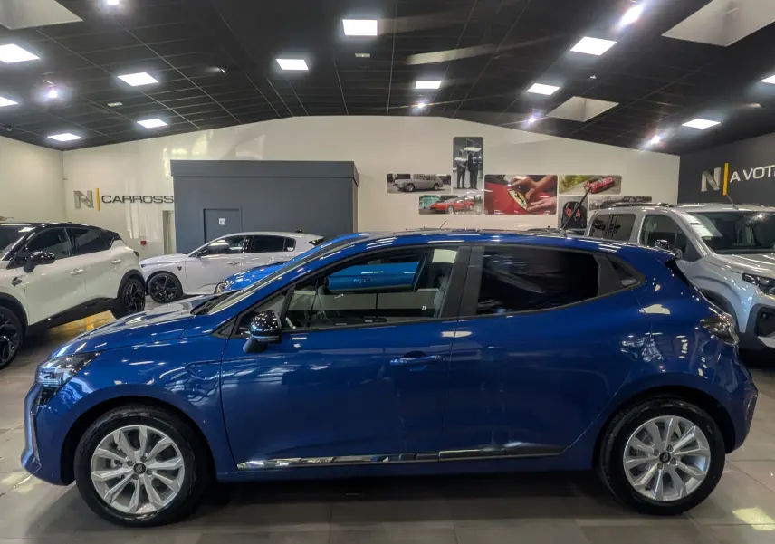 Profil droit d'une Renault Clio V bleu Iron 2025 en intérieur, avec jantes alliage et vitres teintées.