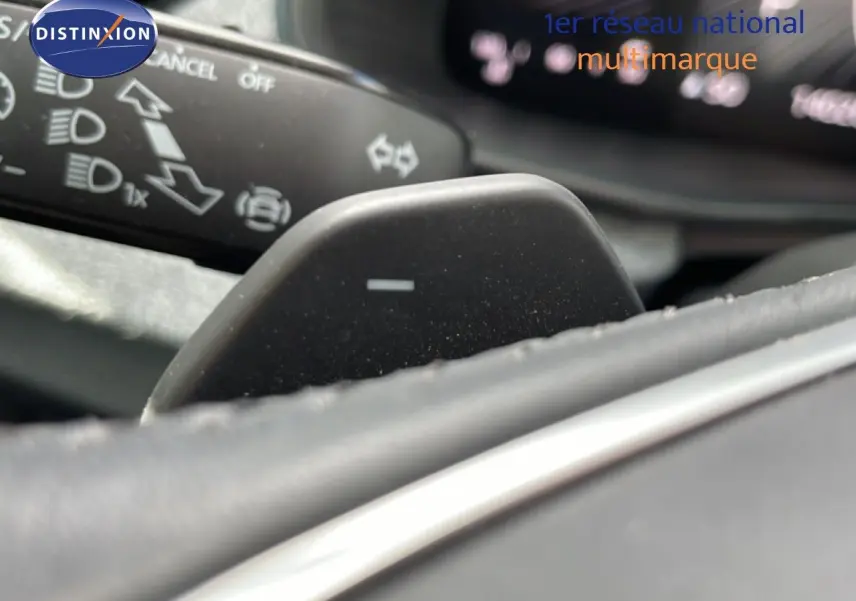 Gros plan sur la palette de changement de vitesse au volant d’une Skoda Scala blanche Glacier, avec commandes au tableau de bord floues.