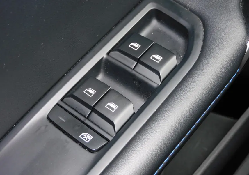 Gros plan sur les commandes de lève-vitres côté conducteur du MG4 blanc, avec surpiqûres bleues sur l'accoudoir noir.