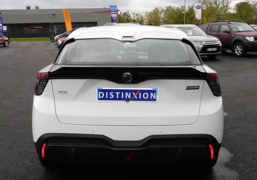 Vue arrière d'une MG4 blanche avec bande noire distinctive sur le hayon et feux arrière LED allumés.