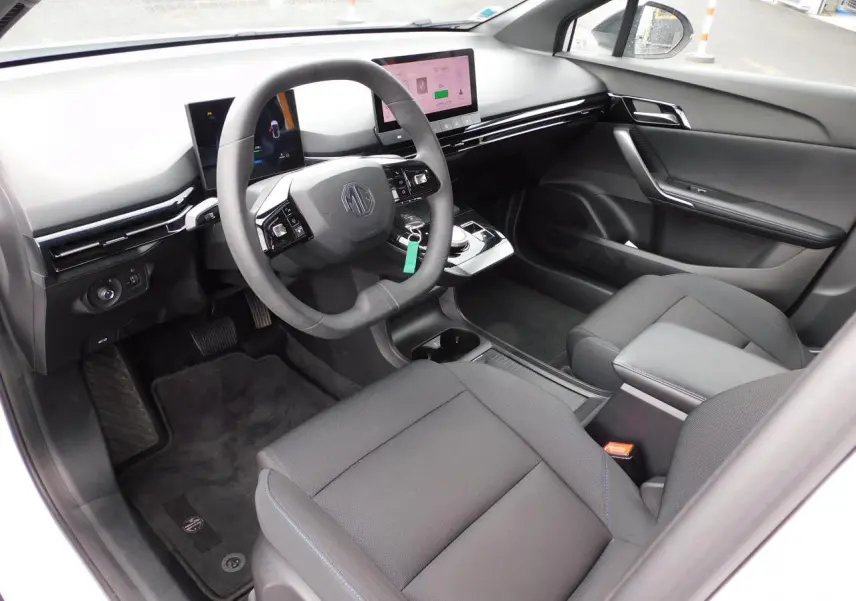 Intérieur noir du MG4 2023 vu côté conducteur, avec volant simili-cuir et écran tactile central lumineux.