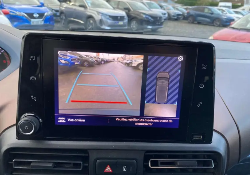Écran de caméra de recul du Peugeot Rifter GT bleu montrant l'arrière et l'angle mort en parking extérieur.