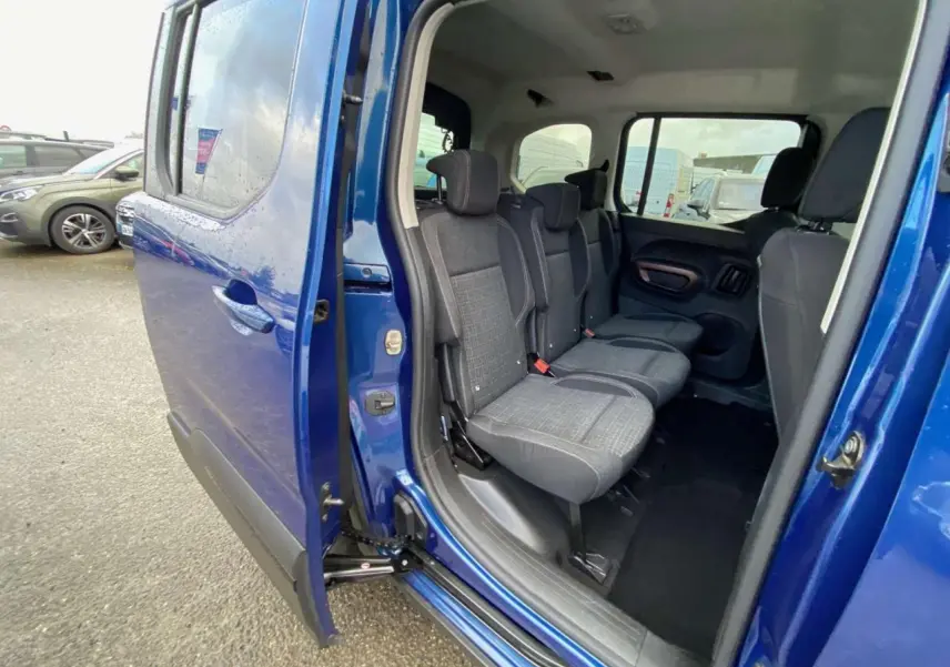 Vue latérale gauche du Peugeot Rifter GT bleu 2023, porte coulissante ouverte montrant les sièges arrière en tissu gris.