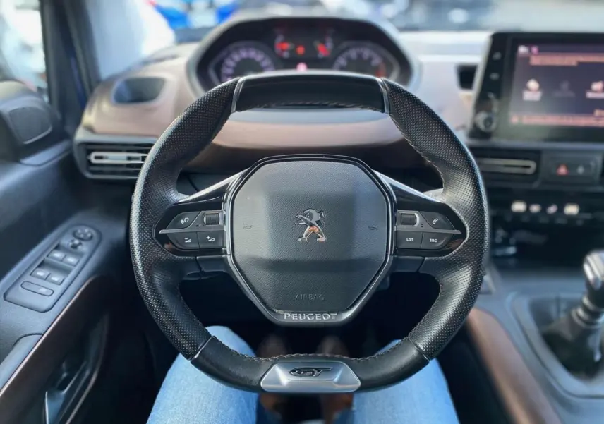 Volant GT noir en cuir avec logo Peugeot, vue centrée depuis le siège conducteur du Rifter bleu 2023.