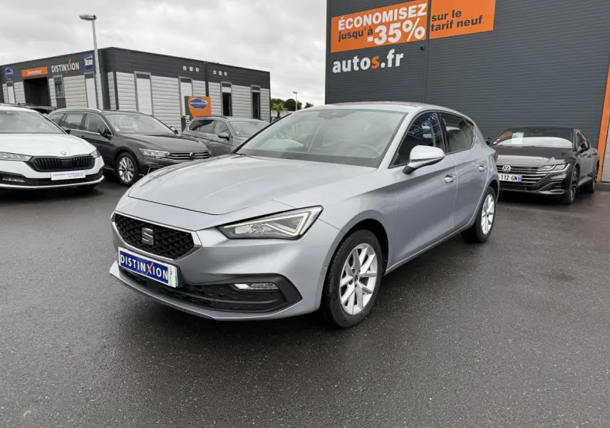 SEAT Leon 2.0 TDI 2022 en gris argenté, vue 3/4 avant droit sur parking devant un bâtiment commercial.