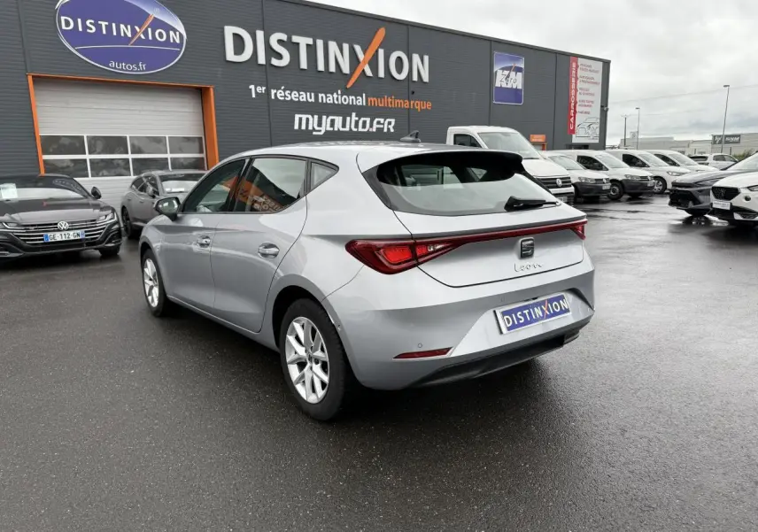 SEAT Leon 2.0 TDI 2022 en gris argenté Urban, vue 3/4 arrière droit sur parking humide devant concession.