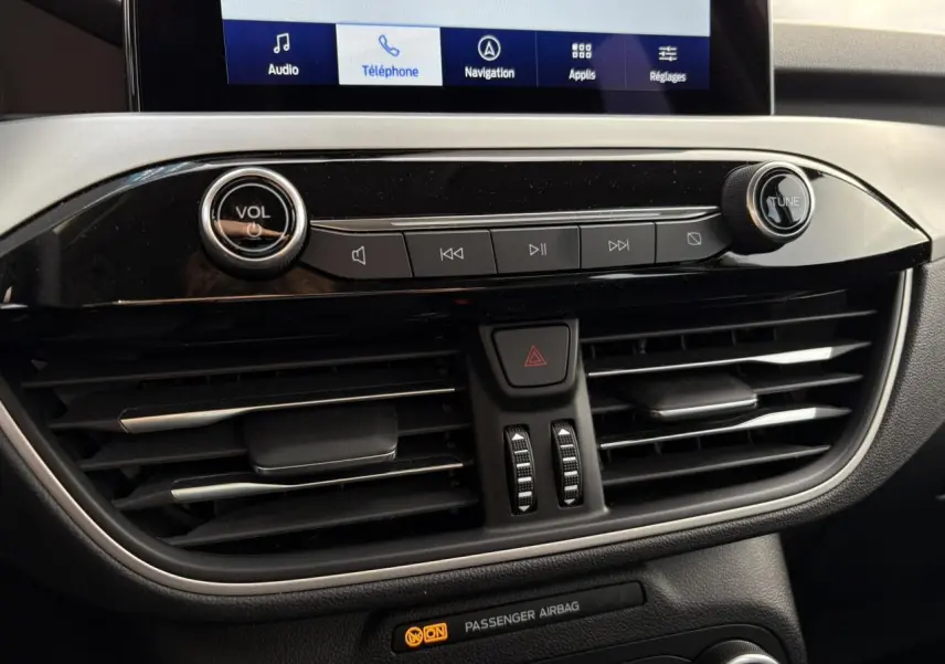 Détail de la console centrale du Ford Kuga 2024 avec commandes audio, ventilation et écran tactile affichant le menu navigation.