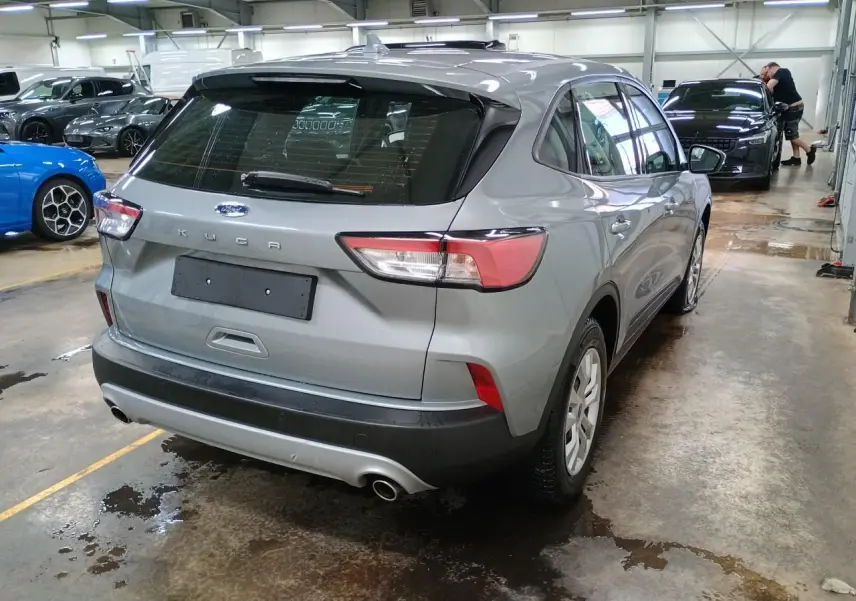Vue 3/4 arrière du Ford Kuga 2024 gris Solar dans un garage, avec feux arrière et double sortie d'échappement visibles.