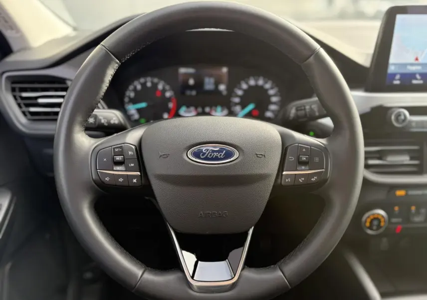 Vue rapprochée du volant en cuir noir du Ford Kuga 2024 avec commandes multifonctions et tableau de bord flou en arrière-plan.