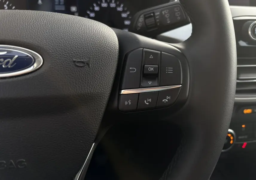 Gros plan sur le volant multifonctions en cuir du Ford Kuga 2024, avec commandes intégrées et tableau de bord en arrière-plan.