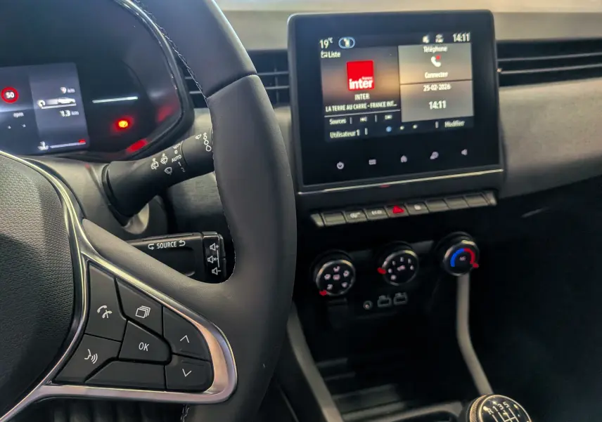 Vue intérieure centrée sur le volant et la console centrale d'une Renault Clio V Bleu Iron avec boîte manuelle et écran tactile.