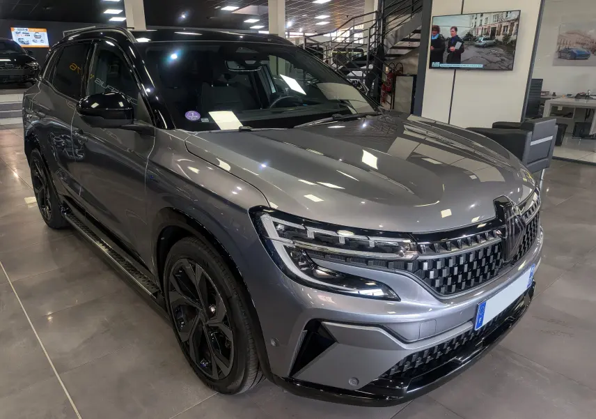 Renault Austral E-Tech hybride gris schiste avec toit noir, vue 3/4 avant droit en intérieur showroom.