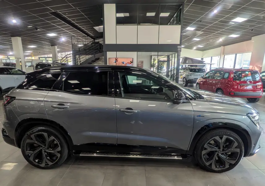 Vue de profil droit du Renault Austral E-Tech hybrid 200 Iconic esprit Alpine en gris schiste avec toit noir dans un showroom.