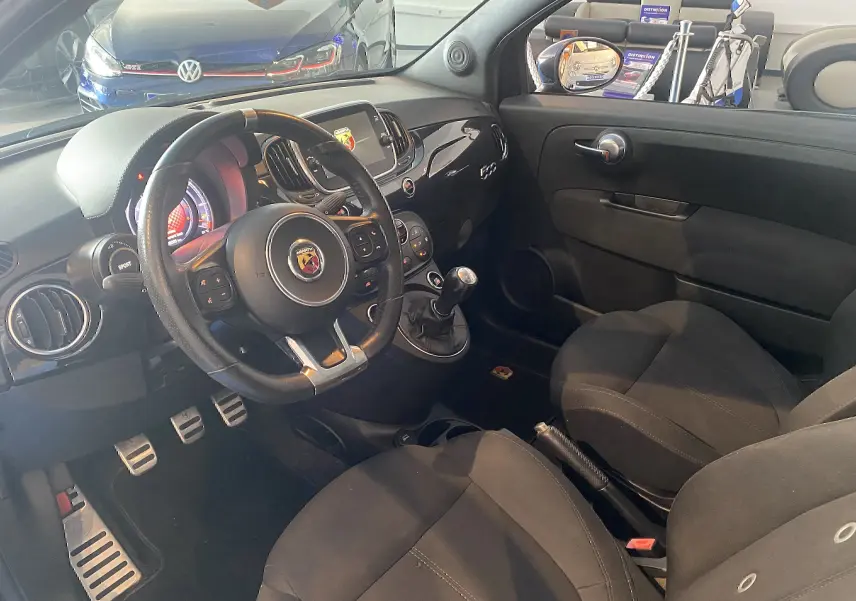 Intérieur noir de l'Abarth 595 2018 vu côté conducteur, volant sport, tableau de bord avec écran et levier de vitesse manuel.