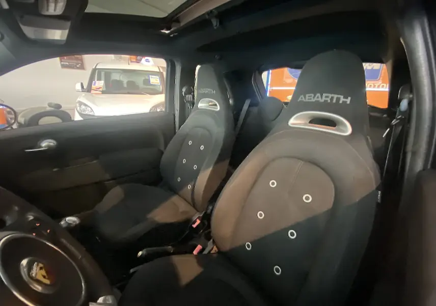 Vue intérieure montrant les sièges avant noirs sport ABARTH avec logo brodé, toit ouvrant partiellement visible.
