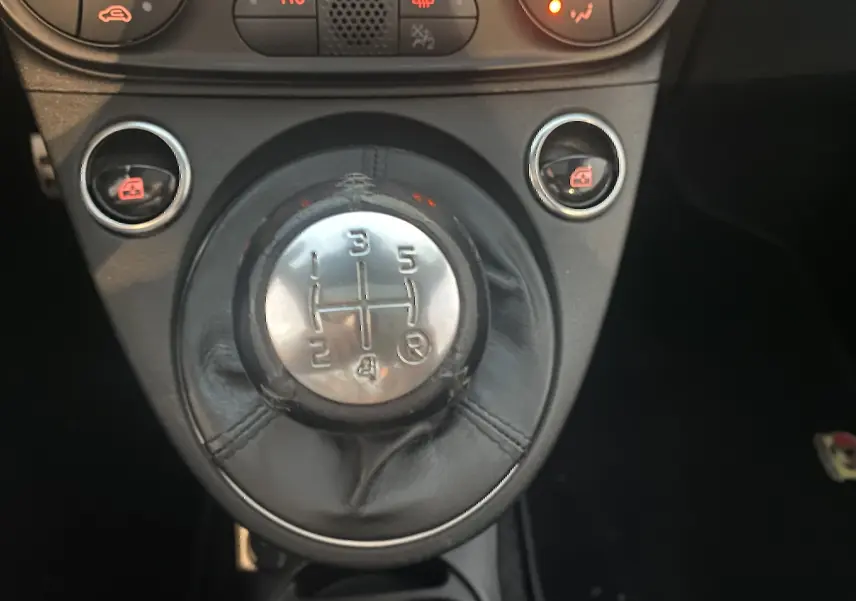 Gros plan sur le levier de vitesses manuel noir de l'Abarth 595 2018 avec boutons de commande et console sombre.