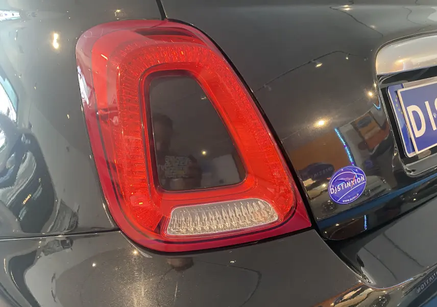Gros plan sur le feu arrière gauche d'une ABARTH 595 noire, avec reflet intérieur et autocollant Distinxion sur le coffre.