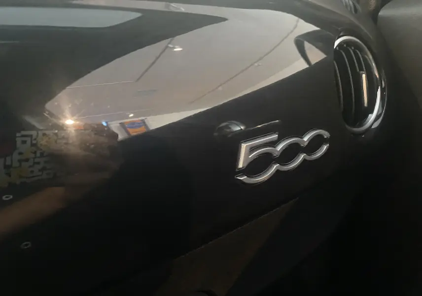 Gros plan sur le tableau de bord noir brillant avec logo 500 et une sortie d'air ronde à droite dans un Abarth 595 2018.