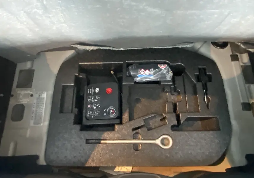 Gros plan sur le coffre d’un Abarth 595 noir de 2018 montrant le kit de réparation et les outils de bord.